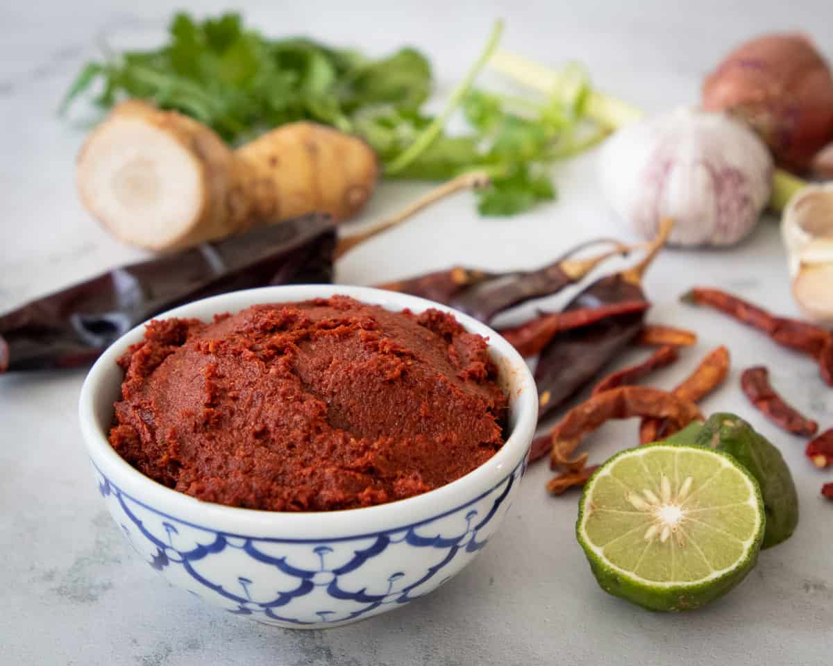 a bowl of red curry paste with ingredients in the background