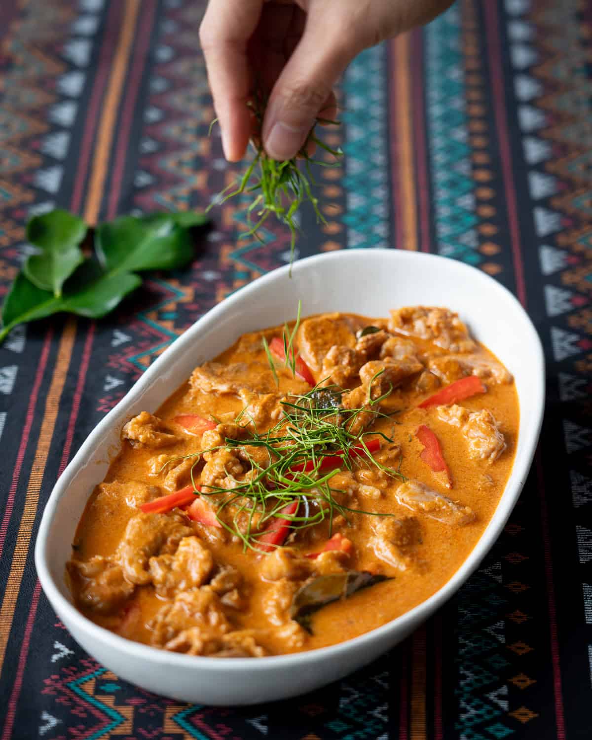 a bowl of panang curry with julienned makrut lime leaves being sprinkled on.