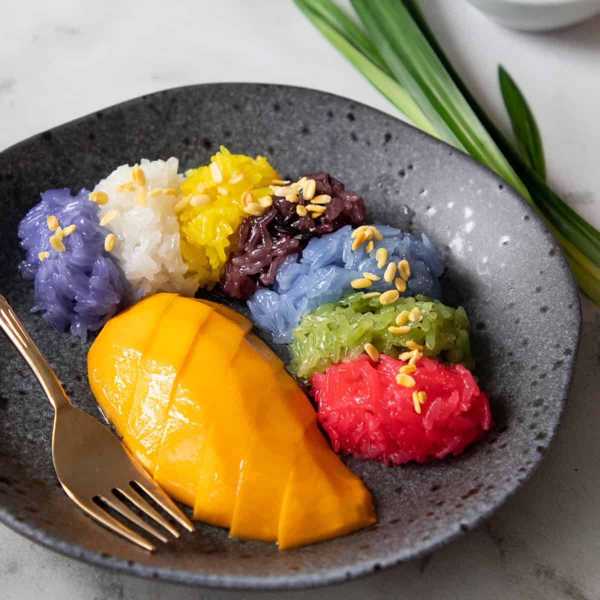 a plate of mango with 7 colours of sticky rice with  mung beans on top.