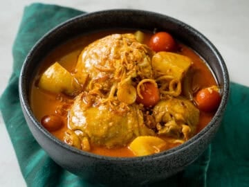 a bowl of yellow curry chicken with cherry tomatoes and potatoes