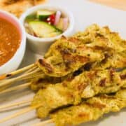 a plate of pork satay with peanut sauce and pickles