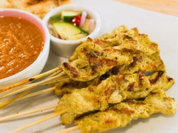 a plate of pork satay with peanut sauce and pickles