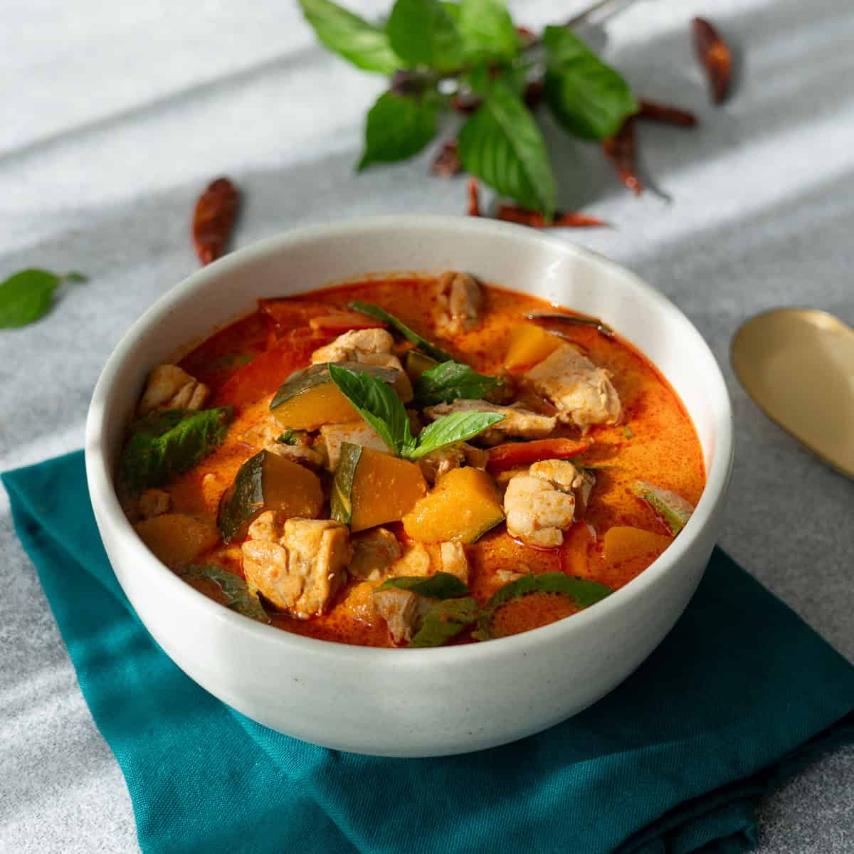 a bowl of red curry with kabocha with thai basil in the background