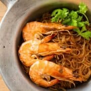 glass noodles with shrimp and cilantro on top in an aluminum pot.