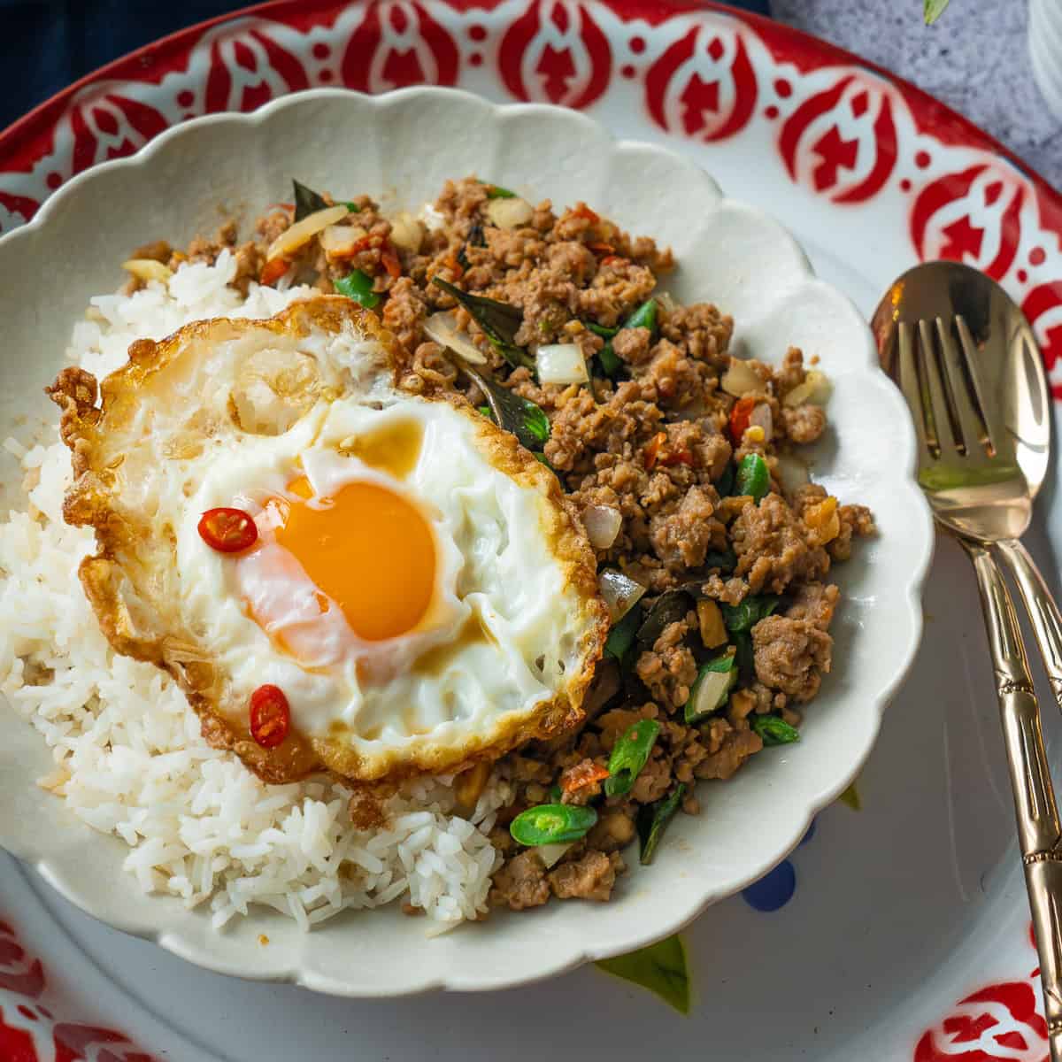 a plate of pad gaprao on rice topped with a fried egg.