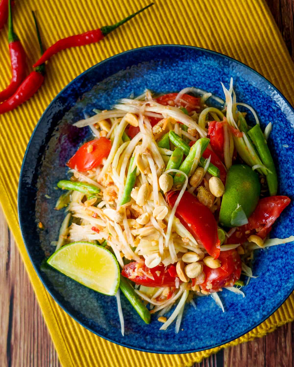 a plate of green papaya salad with a wedge of lime and chilies on the side.