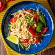 a plate of green papaya salad with a wedge of lime and chilies on the side.