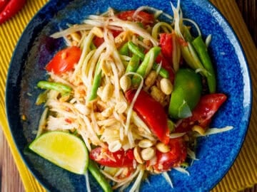 a plate of green papaya salad with a wedge of lime and chilies on the side.