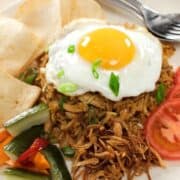 a plate of nasi goreng with a fried egg on top, tomato slices, pickles and shrimp crackers