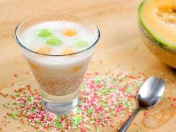 tapioca melon coconut dessert in a glass cup with tapioca pearls and a cantaloupe in the background
