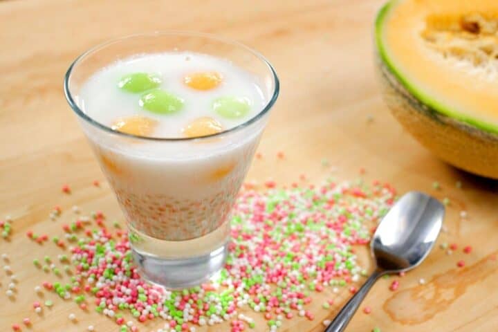 tapioca melon coconut dessert in a glass cup with tapioca pearls and a cantaloupe in the background
