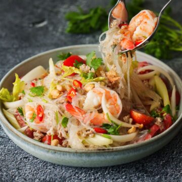 a bowl of yum woon sen with a fork and a spoon picking up the noodles