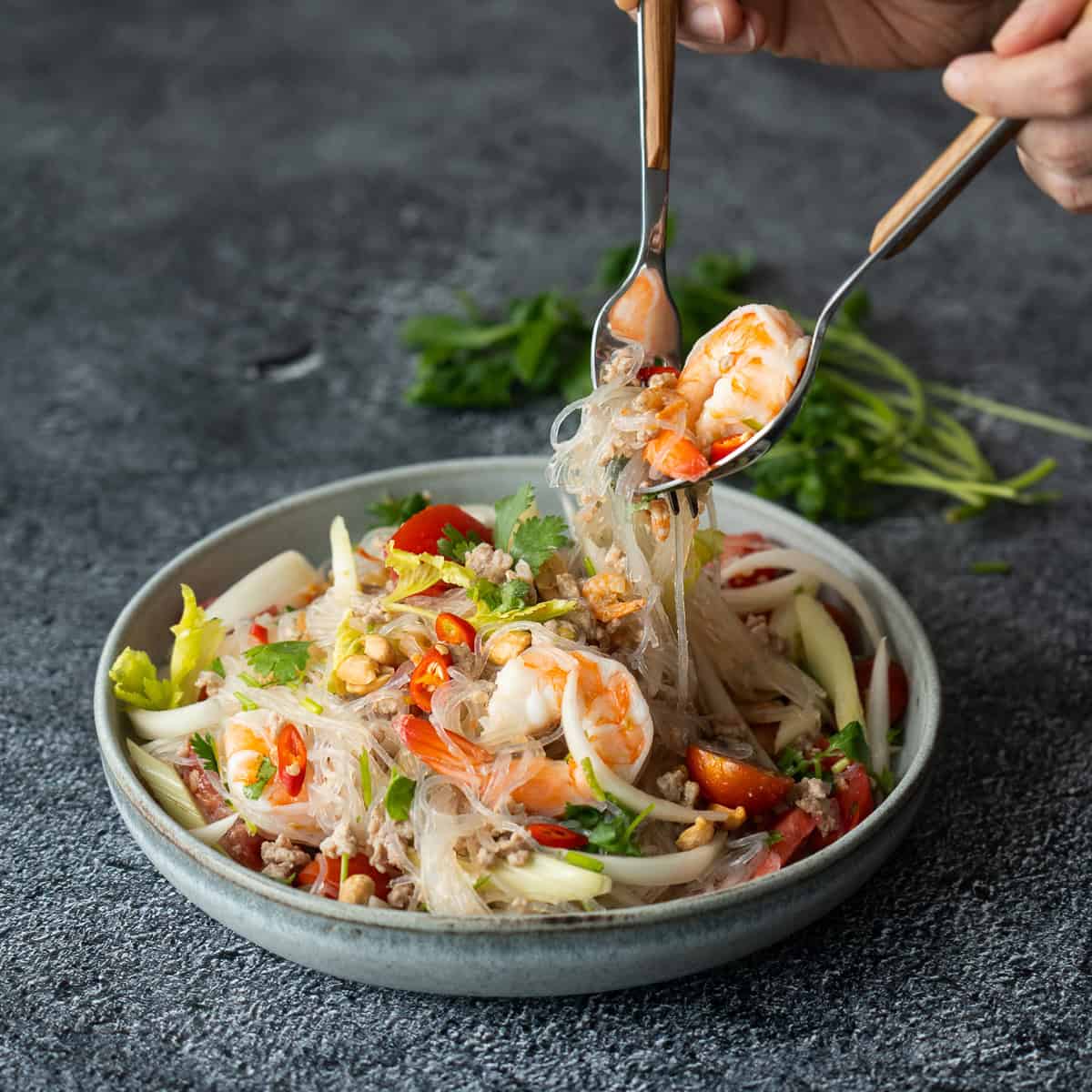 a bowl of yum woon sen with a fork and a spoon picking up the noodles