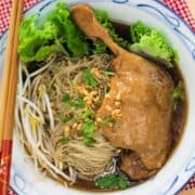 a bowl of duck noodle soup with lettuce and bean sprouts.