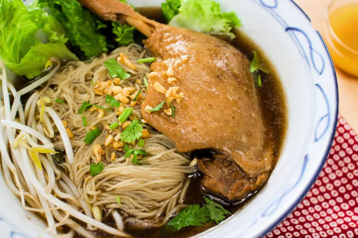 a bowl of duck noodle soup with lettuce and beansprouts.