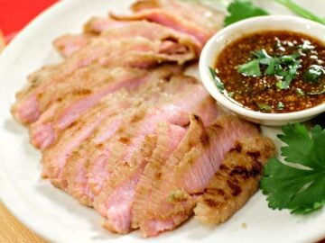 A plate of grilled pork jowl with a side of dipping sauce