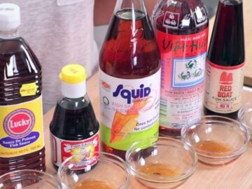 a row of 5 fish sauce bottles with small bowls of fish sauce in front of them