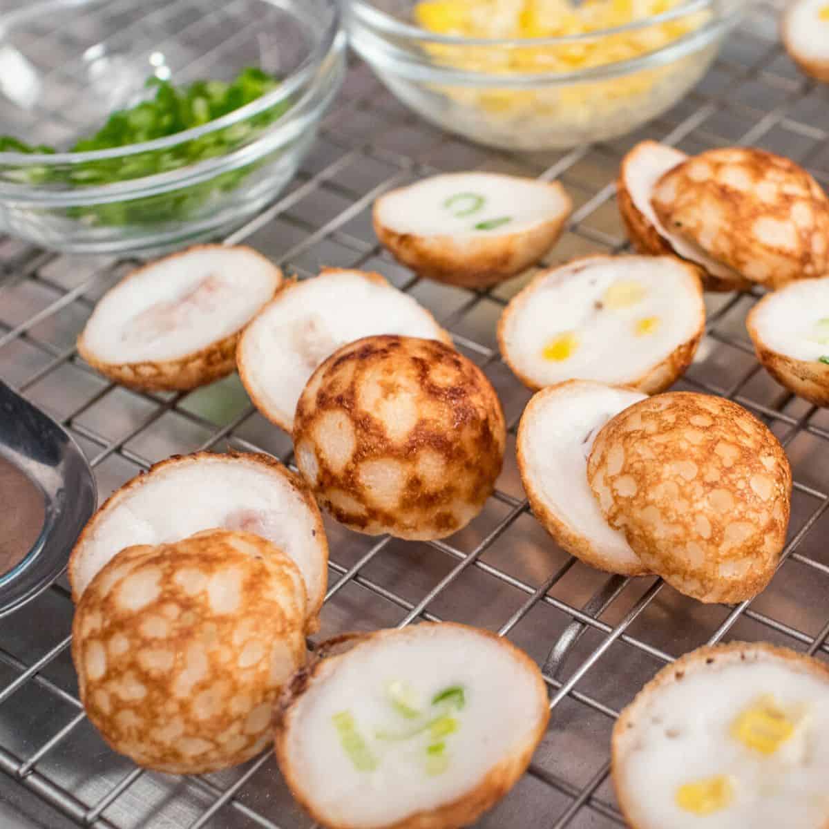 kanom krok pieces on a rack with bowls of green onions and corn