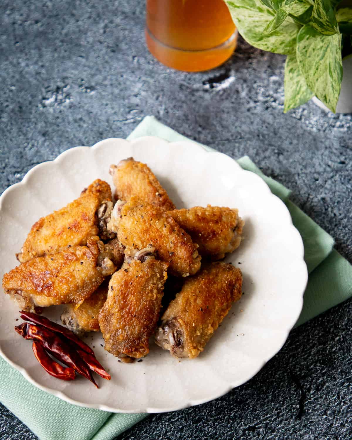 a plate of fish sauce wings with dried chilies garnish and a plant and a beer in the background.