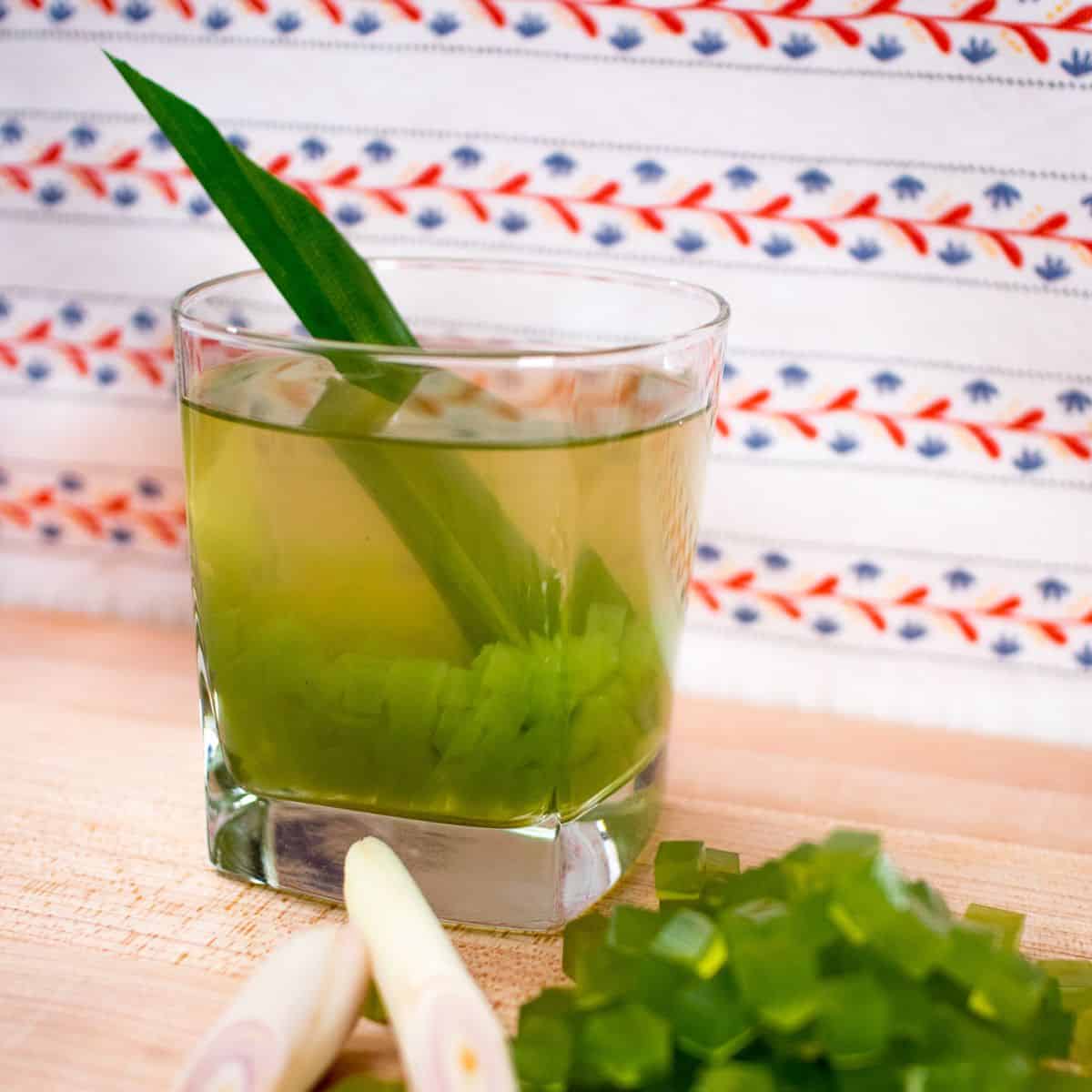 a glass of pandan tea with jelly with a pile of jelly and lemongrass in front