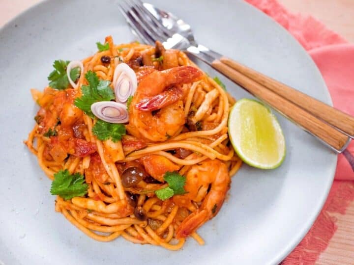 A plate of tom yum spaghetti with shrimp and a wedge of lime
