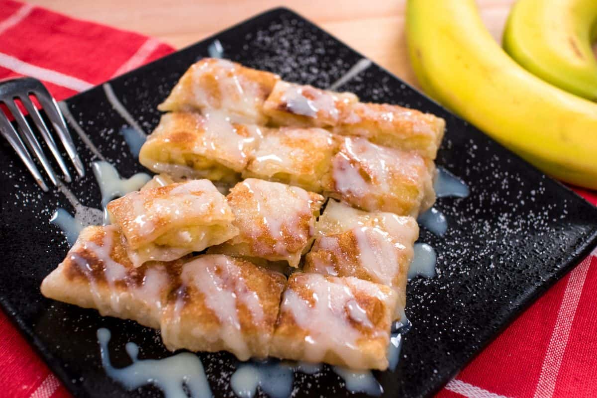 a plate of thai banana roti cut into squares drizzled with condensed milk