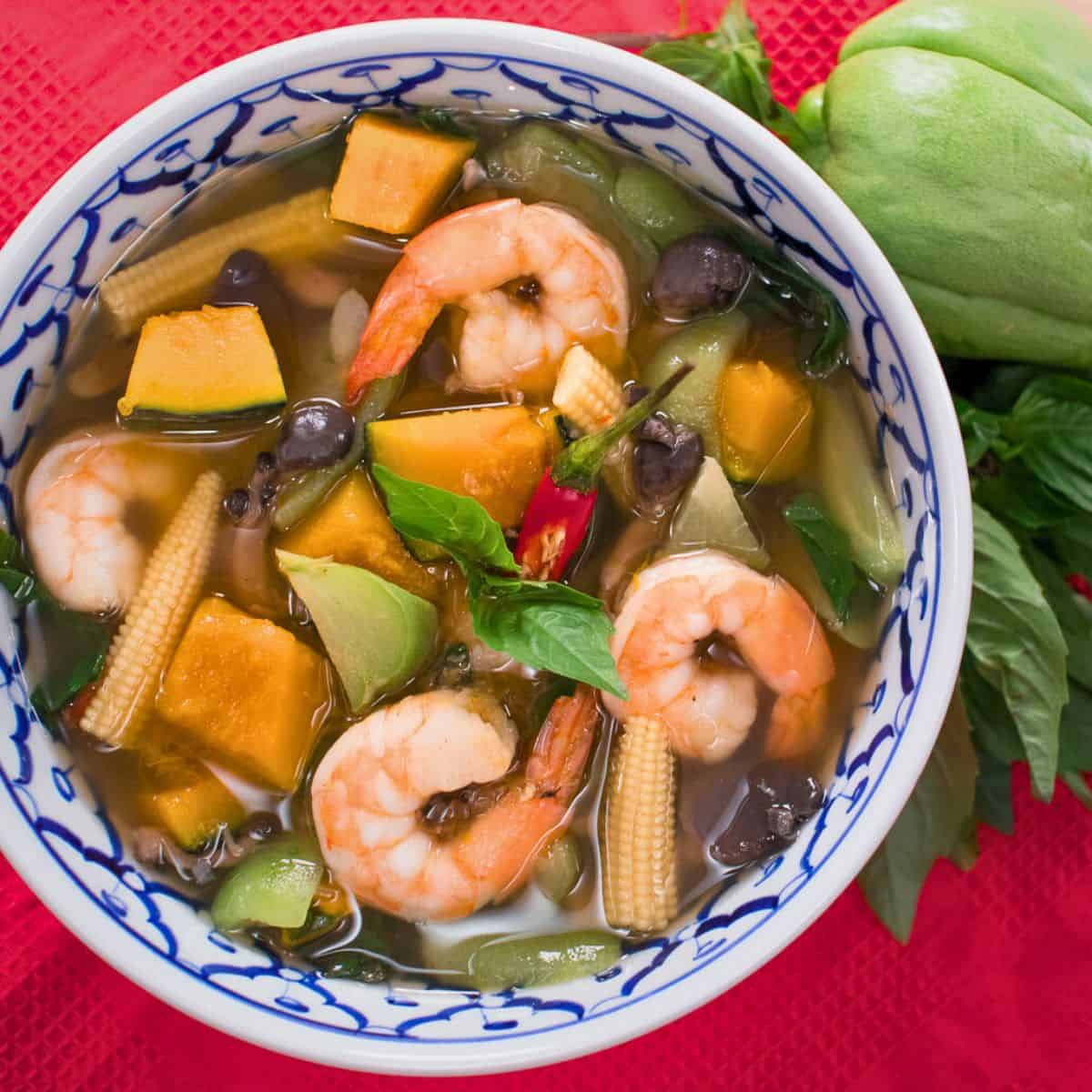 a bowl of gaeng liang with shrimp and veggies with a chayote squash and thai basil on the side.