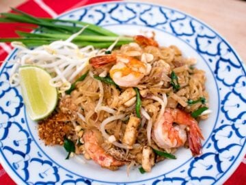 A plate of pad thai with shrimp and a side of lime and bean sprouts