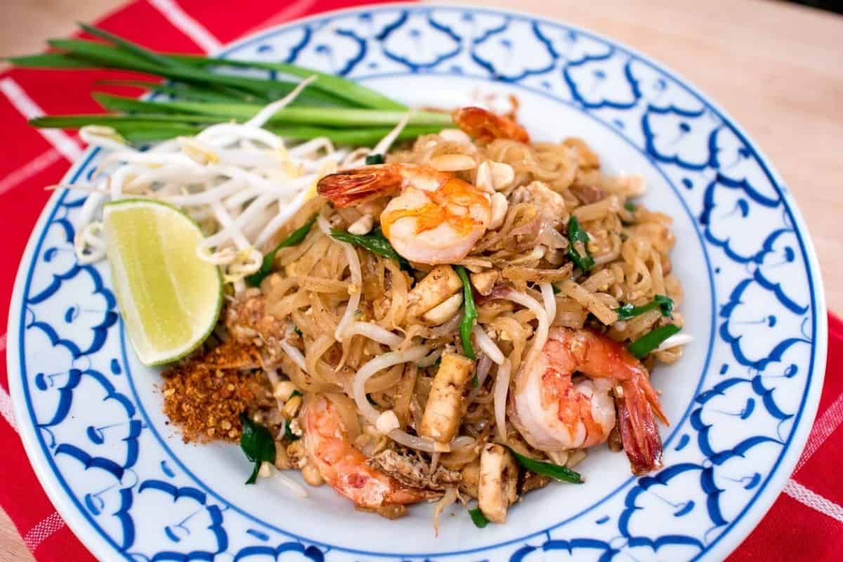 A plate of pad thai with shrimp and a side of lime and bean sprouts