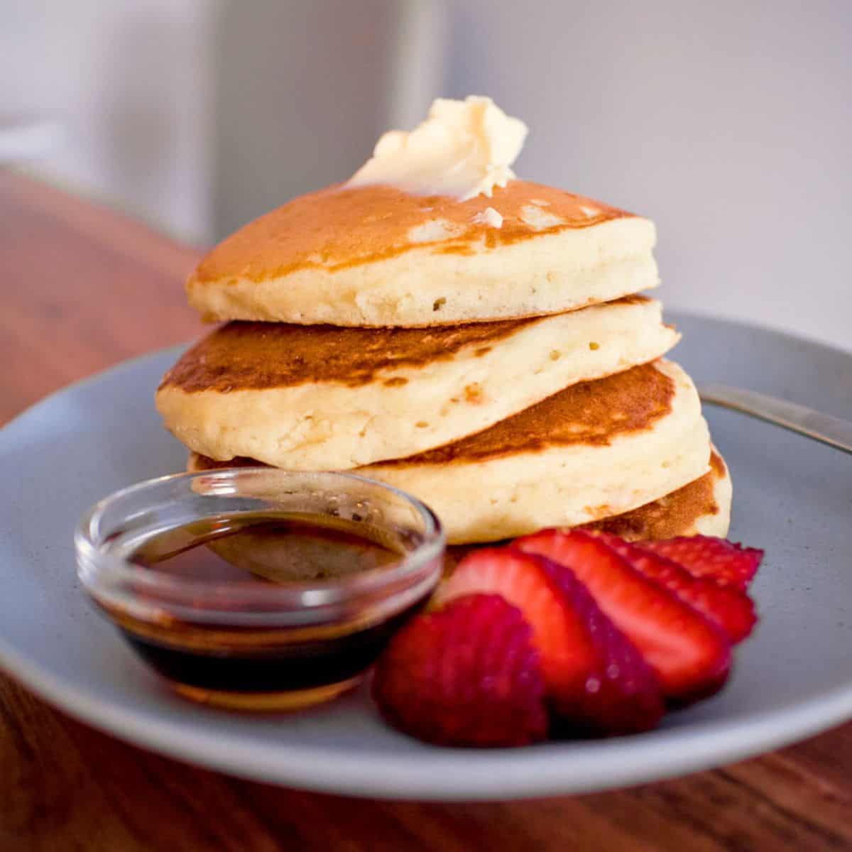 A stack of pancakes with strawberries and maple syrup