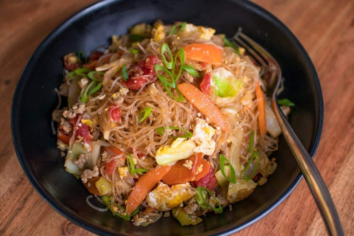 A black bowl of glass noodle stir fry.