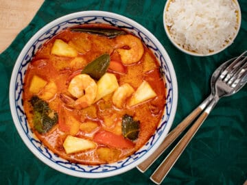 A bowl of pineapple curry with shrimp and a side of rice