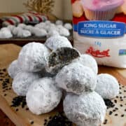 A pile of black sesame snowball cookies on a cutting board