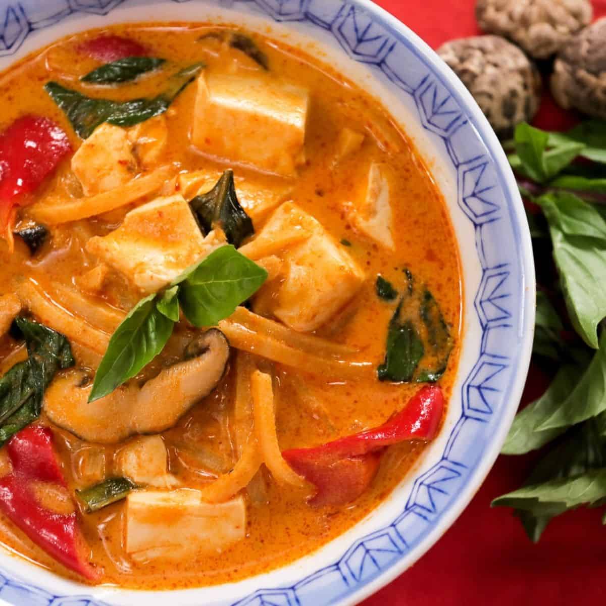 A bowl of Thai red curry with mushrooms, tofu, and Thai basil