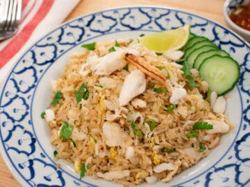 A plate of fried rice with crab, cucumber and lime.