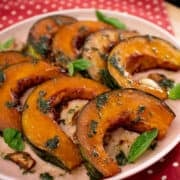 A plate of roasted kabocha squash wedges with basil leaves