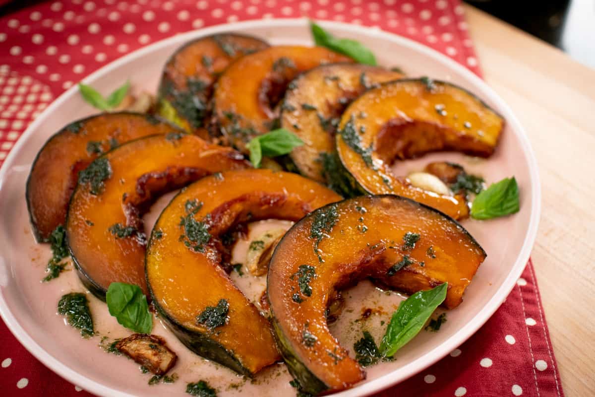 A plate of roasted kabocha squash wedges with basil leaves