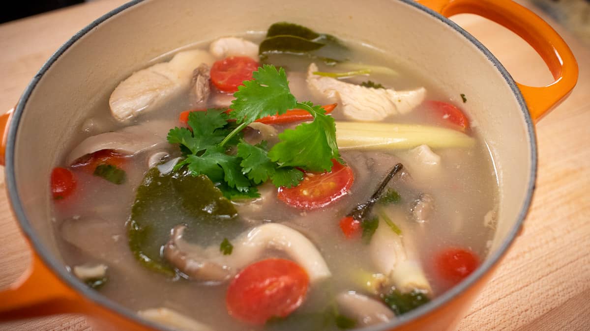 A pot of Thai soup with turkey, mushrooms, and tomatoes with cilantro on top