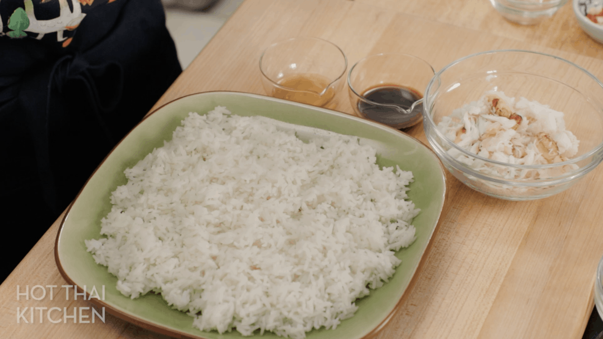 Rice spread out on a plate, with bowls of fish sauce and soy sauce beside it.