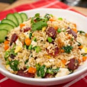 A bowl of chinese sausage fried rice with cucumber garnish on red table cloth