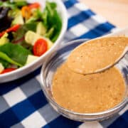A spoonful of roasted sesame dressing being held over a bowl of dressing. With a green salad on the side. sp