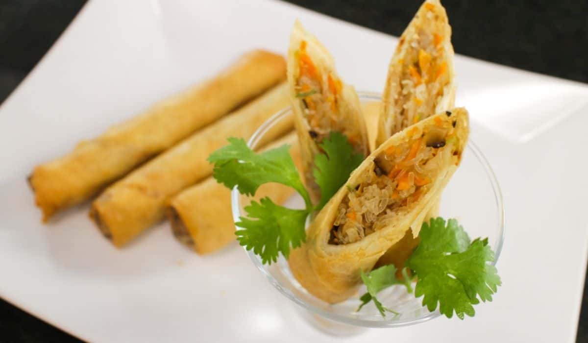A plate of spring rolls, with 3 pieces cut open served in a glass. Cilantro garnish.