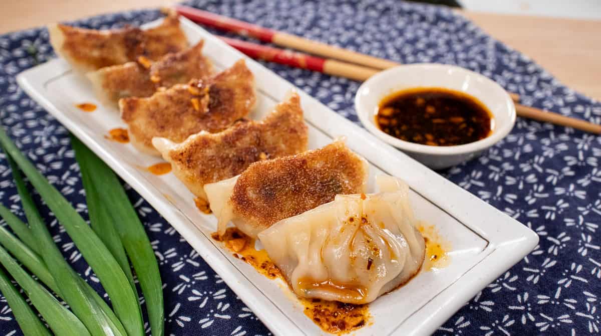 A plate of gyozas with crispy bottoms, with chili oil drizzled on them and dipping sauce on the side.