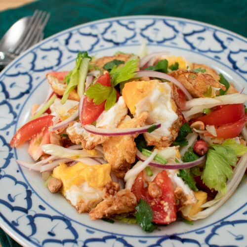 Fried egg salad with tomatoes, onions and celery on a white and blue plate.