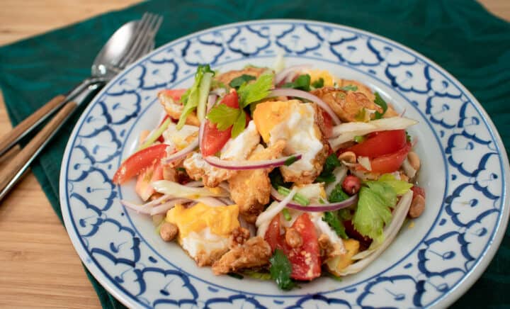 Fried egg salad with tomatoes, onions and celery on a white and blue plate.