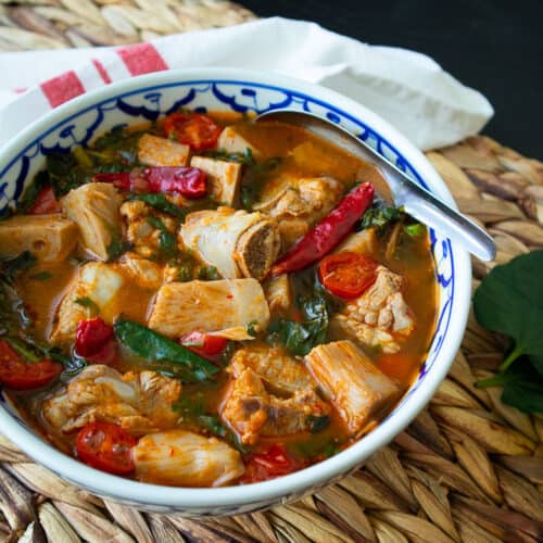 A bowl of ribs and jackfruit curry with chilies, tomatoes, and greens.