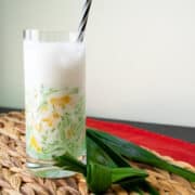 A glass of lod chong singapore with a straw and pandan leaves on the side.