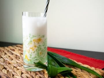 A glass of lod chong singapore with a straw and pandan leaves on the side.