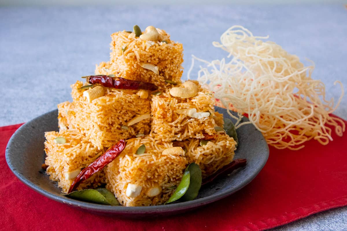 A plate of sweet and sour crispy noodle squares with dried chilies and makrut lime leaves garnishes.
