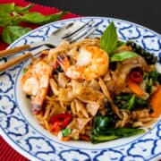 A plate of drunken noodles with shrimp on red placemat